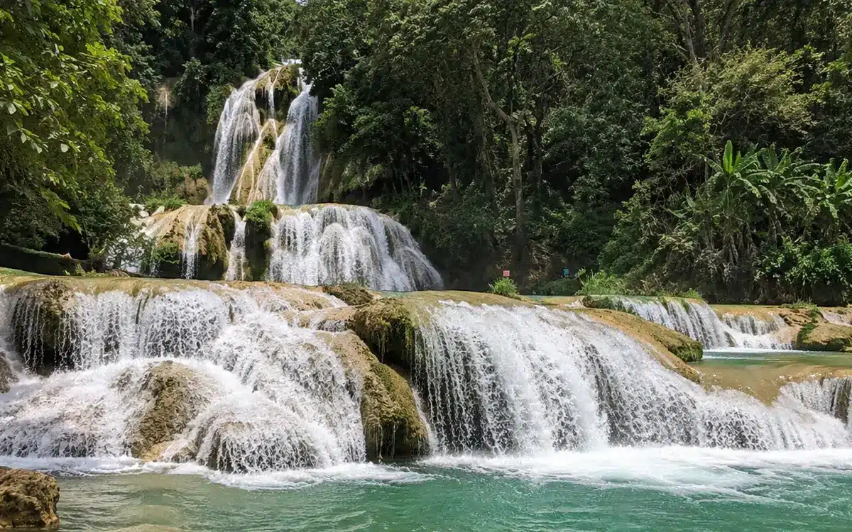 Se ven varias caídas de agua distribuidas en terrazas naturales de roca, creando una vista amplia y fresca.