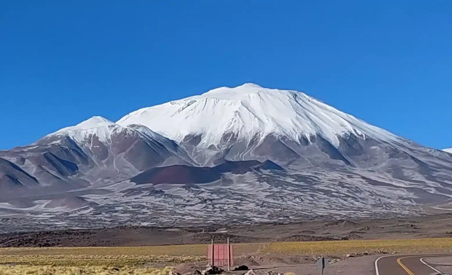 Snow-capped Incahuasi Volcano rising above an arid high-altitude landscape with a paved road in the foreground