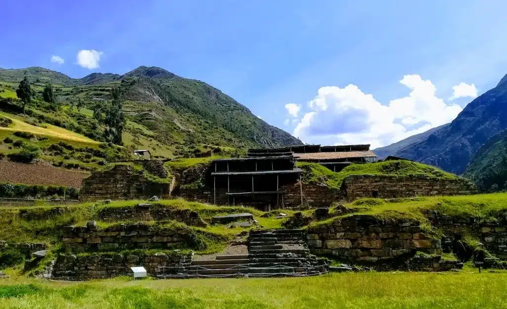 View of Chavín de Huántar stone ruins and terraces in a green Andean valley under a bright blue sky