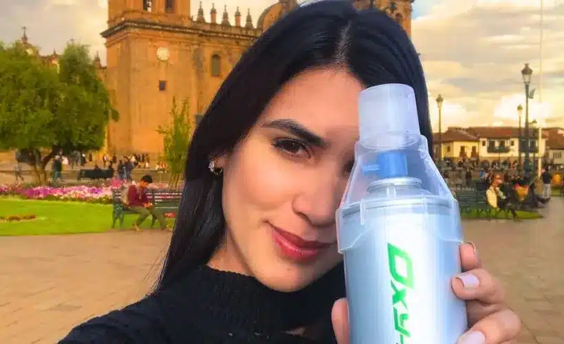 Traveler holding portable oxygen bottle in Cusco’s highlands, demonstrating altitude preparation and importance of flu and tetanus vaccines for Peru’s Andean regions.