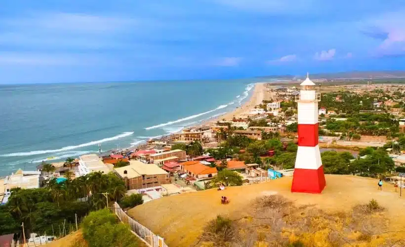 Aerial view of Lima coast with cliffs, highway, and malecón; surfers in the Pacific, pebbled shoreline, and city buildings above the bluffs on Peru’s central coast.