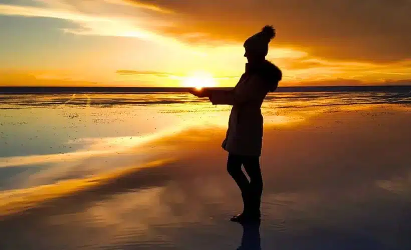 Traveler wearing a winter jacket and beanie at the Uyuni Salt Flats, standing under a clear sky during golden hour, highlighting the need for warm clothes.
