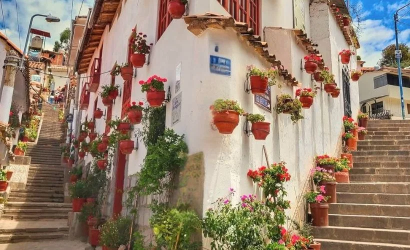 Calle Siete Borreguitos street view from Plaza de Armas showing steep cobblestone stairs, colonial balconies with carved wood details, flower-filled flowerpots, and traditional whitewashed walls making it one of Cusco's most Instagrammable photography locations.