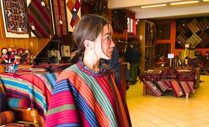 A group of women weavers in Chinchero, Cusco, sit together weaving colorful textiles. They use backstrap looms inside a communal workshop surrounded by local families.