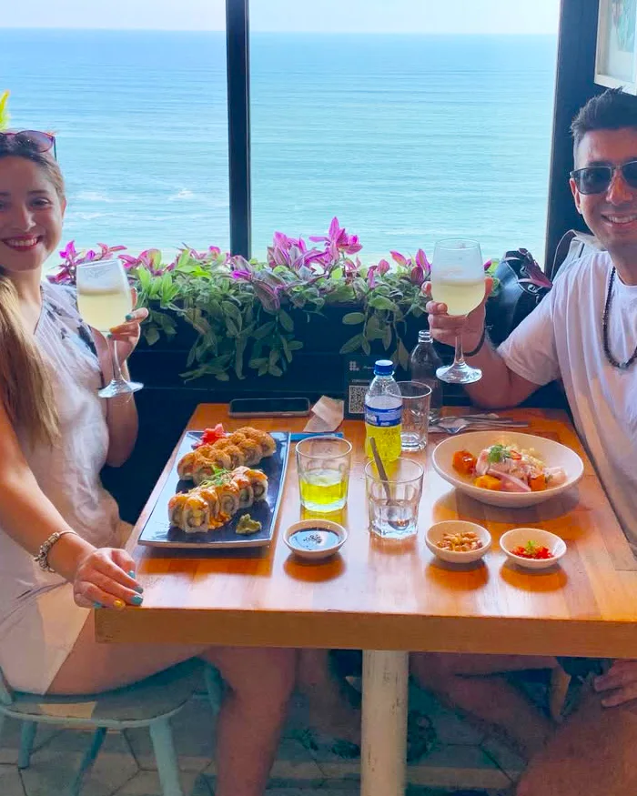 Pareja brinda con pisco sour durante una comida frente al mar en Lima