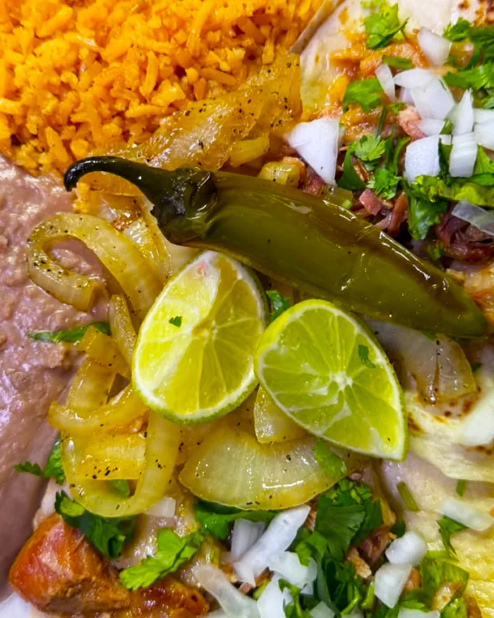 A plate of Mexican carnitas tacos served on warm tortillas with chopped onions, fresh cilantro, and salsa, photographed on a rustic table in a casual street food setting.