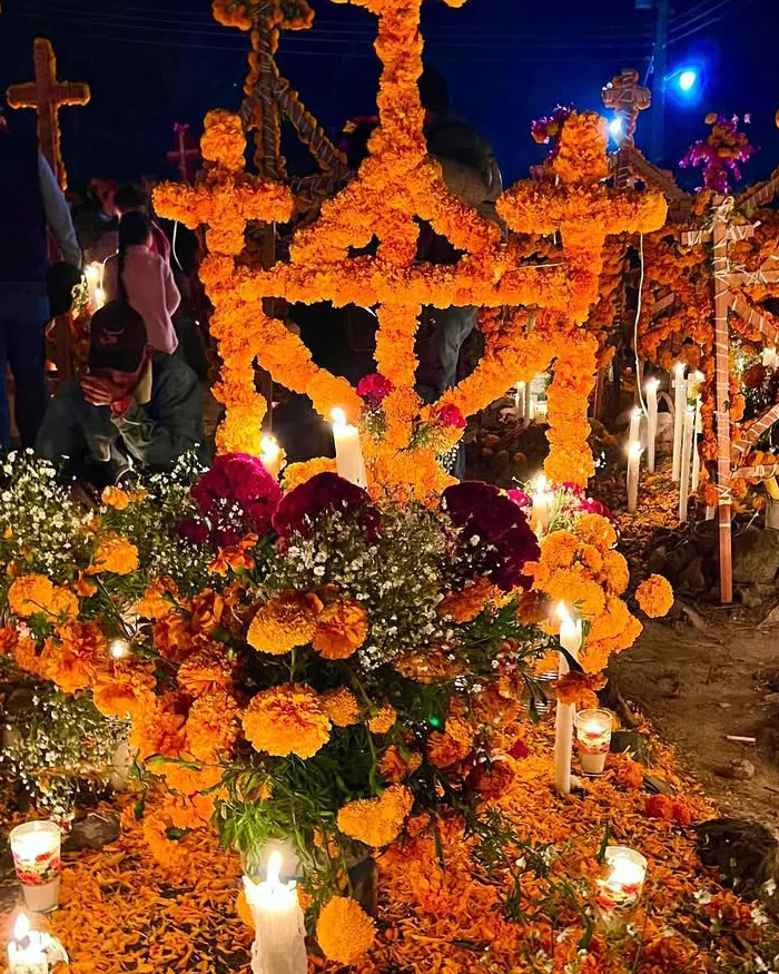 Families gather at night lighting candles around decorated altars in a cemetery, honoring loved ones with flowers, offerings, and traditional rituals during Día de Muertos.