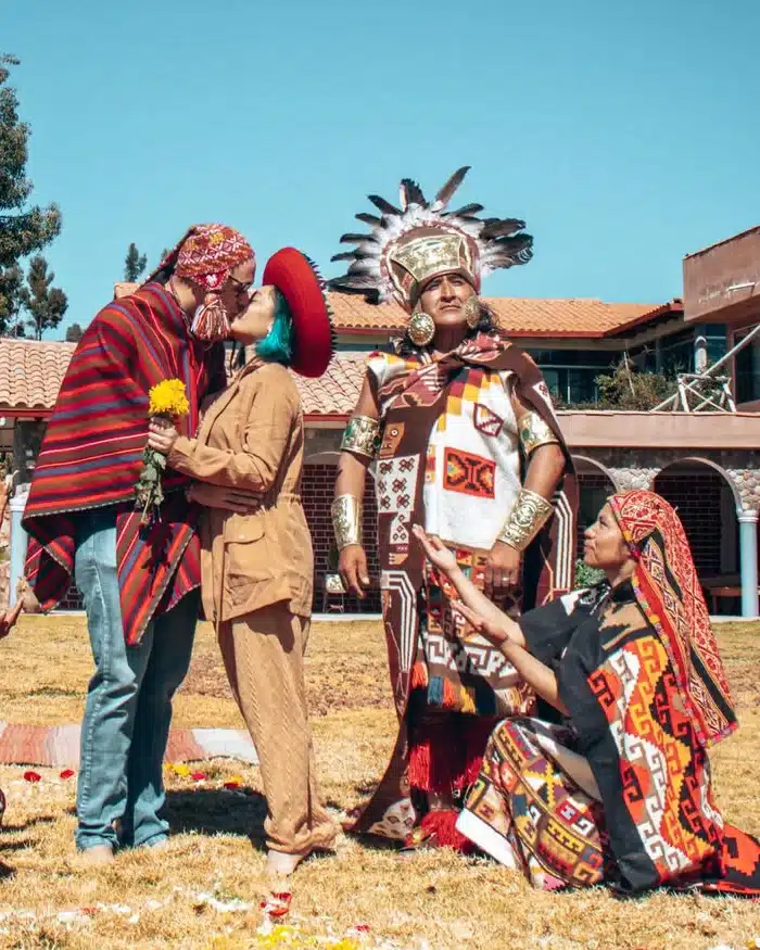 A couple kisses during a traditional Andean ceremony, surrounded by officiants wearing typical clothing, with Andean decorations and cultural elements around them.