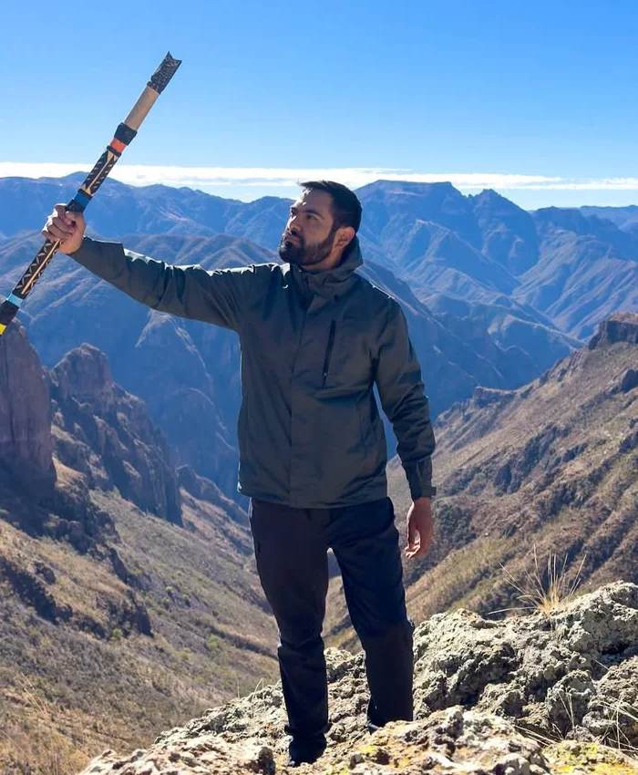 Se observa a un hombre de pie sobre una formación rocosa en lo alto de una montaña.