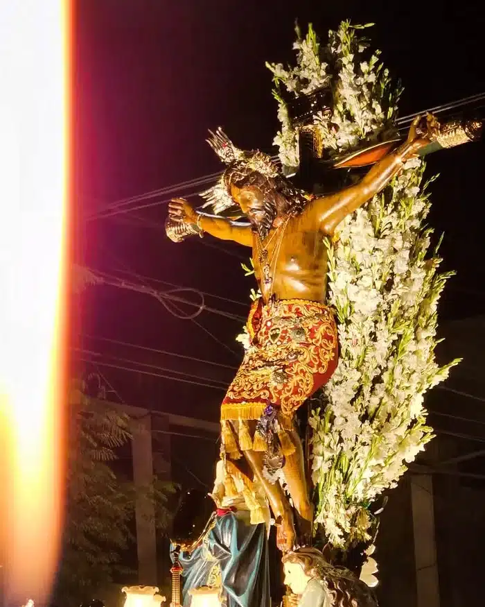 Una procesión nocturna muestra al Cristo crucificado con vestimenta bordada.