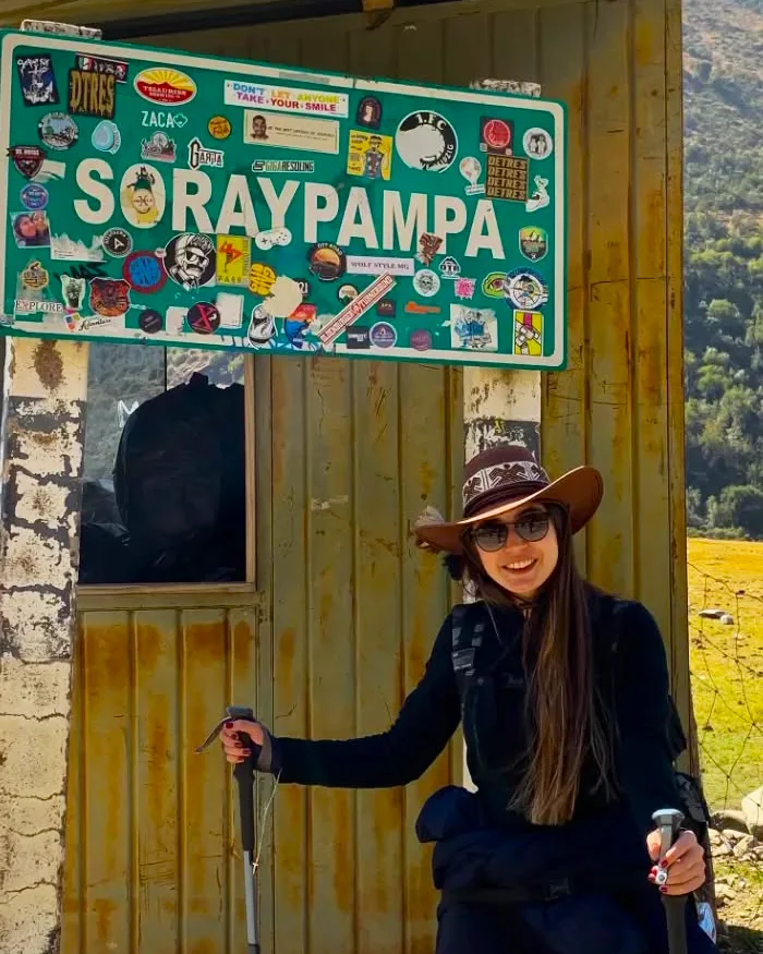 Una viajera sonríe frente al cartel de Soraypampa, punto de inicio del famoso trekking hacia el nevado Salkantay.