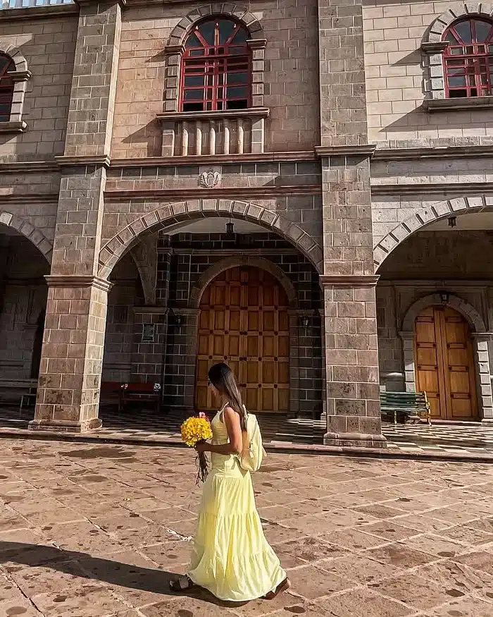 A colonial temple with stone arches and a tall bell tower stands under a bright blue sky, highlighting Cusco’s historic religious architecture.