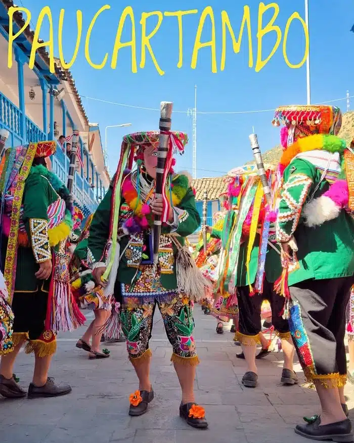 Traditional dancers perform ancestral steps in a lively square filled with spectators, fireworks smoke, and colorful Andean costumes during a cultural festival.