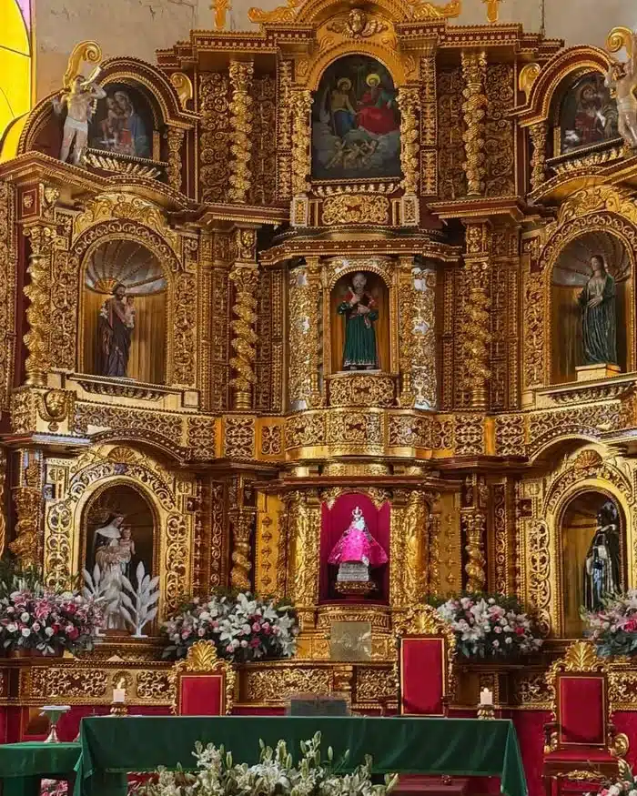 A richly decorated golden baroque altar displays carved religious details illuminated by warm light inside a historic Andean church in Cusco.