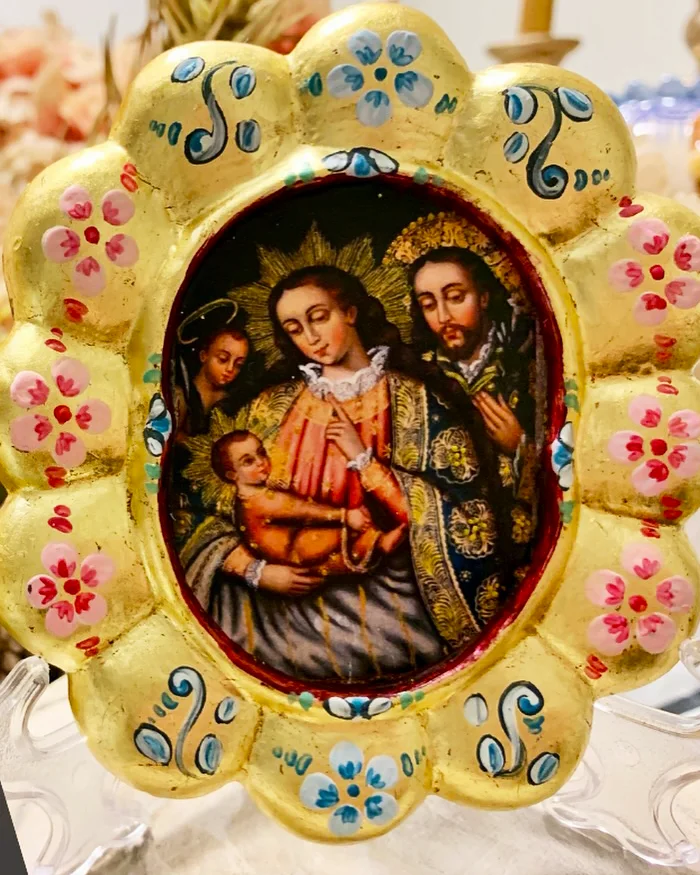 El marco dorado está decorado con flores pintadas en tonos rosados, azules y celestes.