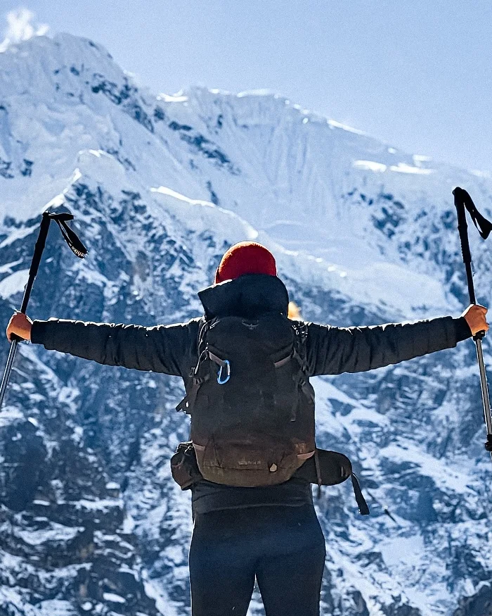 A traveler in trekking gear faces the towering snow-capped Salkantay Mountain, with rocky slopes and bright skies framing one of Cusco’s most iconic peaks.