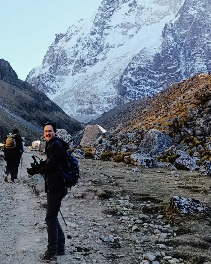 A lone hiker walks along a rocky Andean trail near Salkantay, surrounded by sparse vegetation, steep terrain, and cold high-altitude conditions common on Cusco trekking routes.