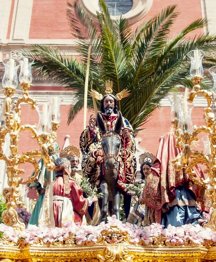 La escena está rodeada de otras figuras religiosas vestidas con túnicas detalladas y bordados dorados.