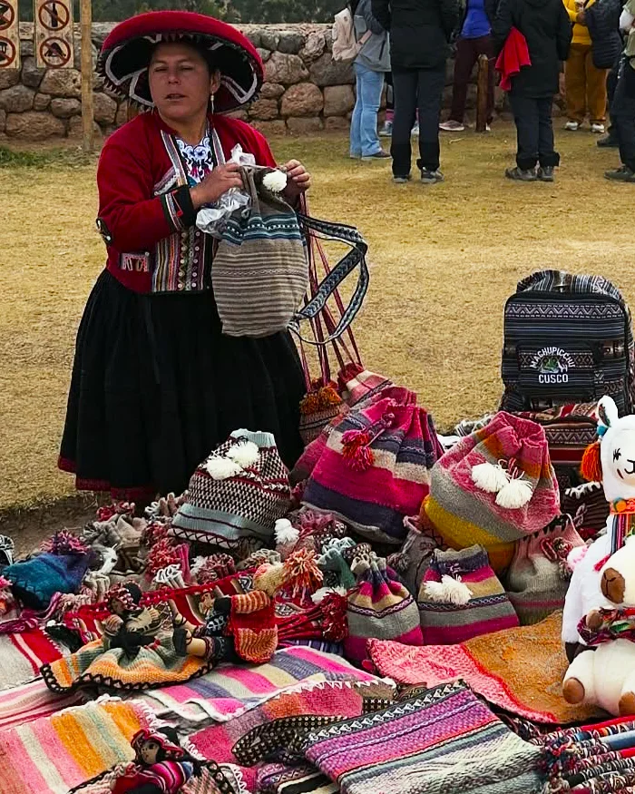 La vendedora, vestida con un traje tradicional de colores vivos, sostiene una prenda de lana mientras espera a los visitantes.