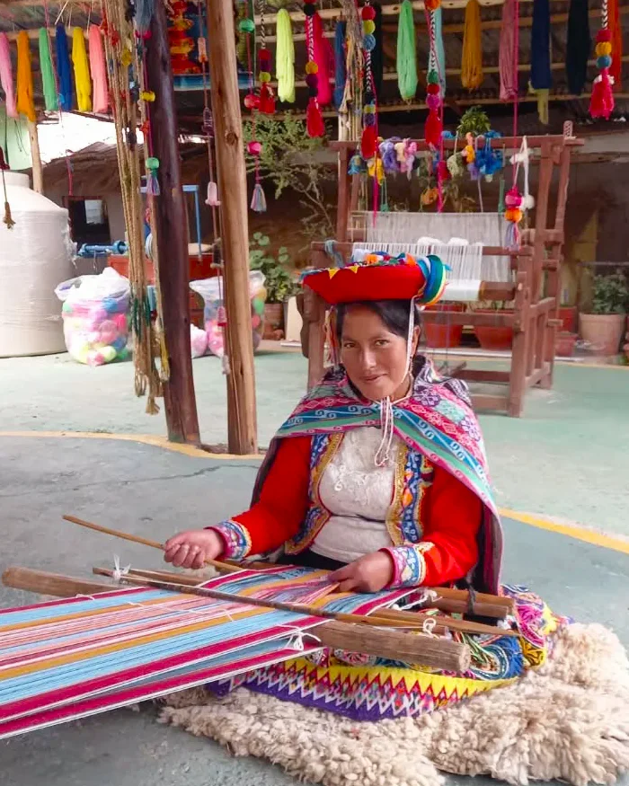 La mujer sostiene con habilidad los palos del telar, concentrada en la creación de un tejido multicolor.