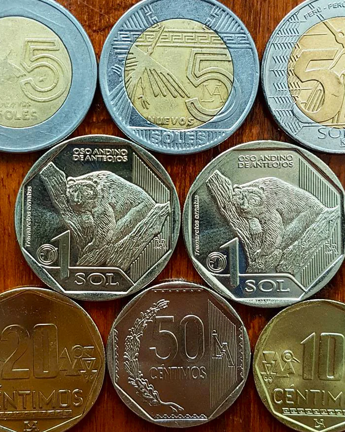 Assorted Peruvian coins arranged on a surface showing geometric engravings, national motifs, and metallic finishes used in daily transactions throughout Cusco and the Sacred Valley.