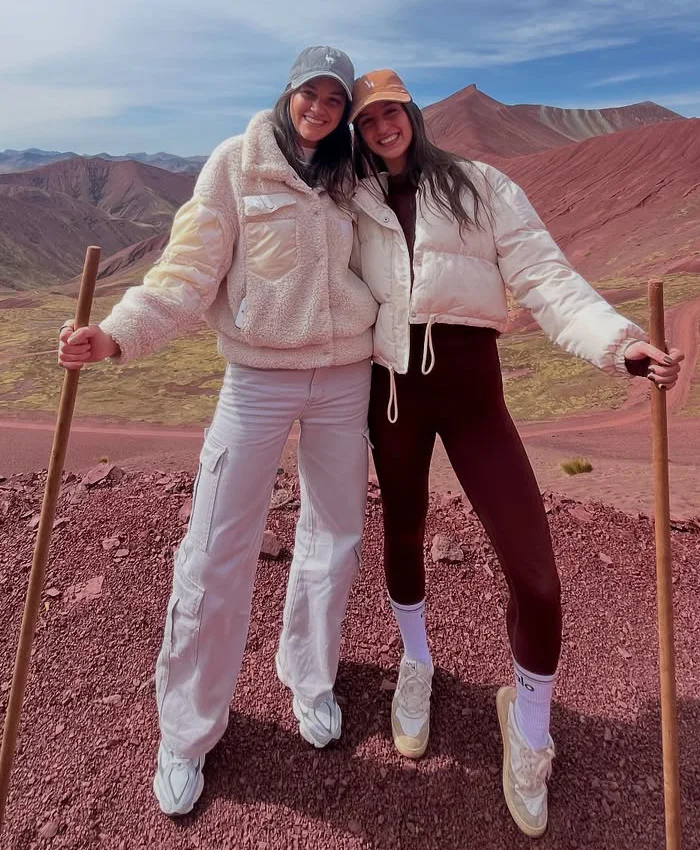 Se observa a dos mujeres sonrientes posando juntas en un paisaje montañoso de tonos rojizos.