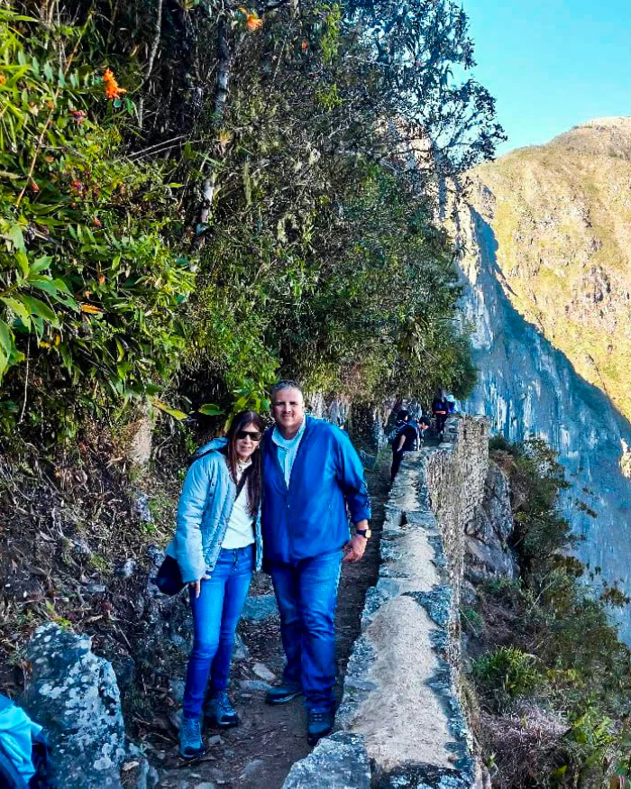 Una pareja de turistas posa abrazada en un estrecho sendero rodeado de naturaleza.