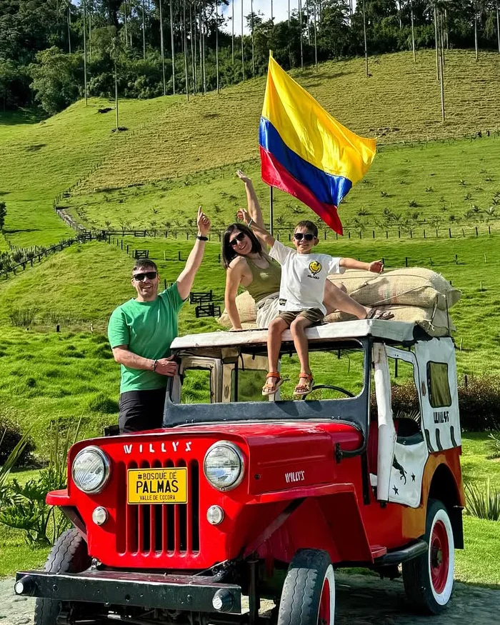Una familia disfruta un momento inolvidable posando sobre un clásico Willys rojo en medio del Valle de Cocora.