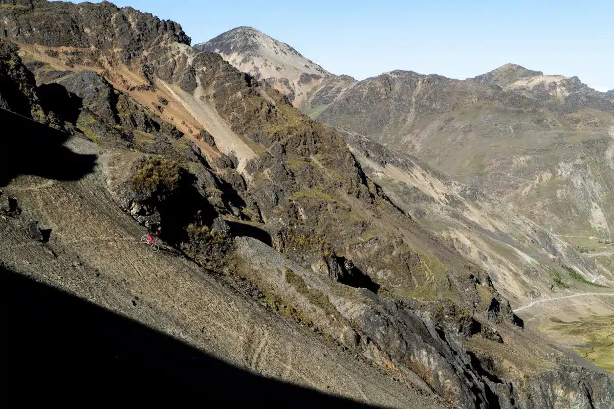 Ciclista cruzando un sendero rocoso de montaña en la ruta de Lares, Cusco, rodeado de valles profundos y picos andinos elevados (Peru Biking Tours).