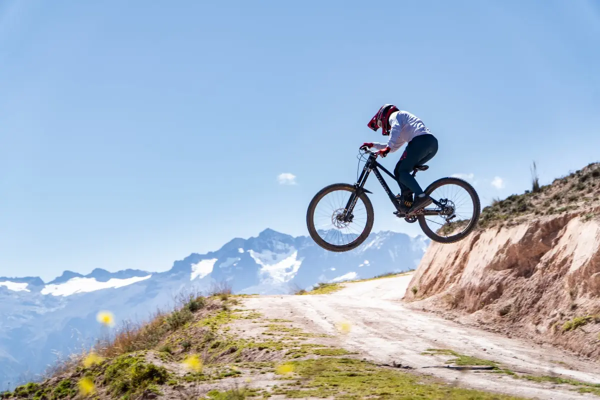 Ciclista realizando un salto en rutas de alta montaña con vistas panorámicas a la cordillera del Vilcanota bajo un cielo azul despejado (Peru Biking Tours).