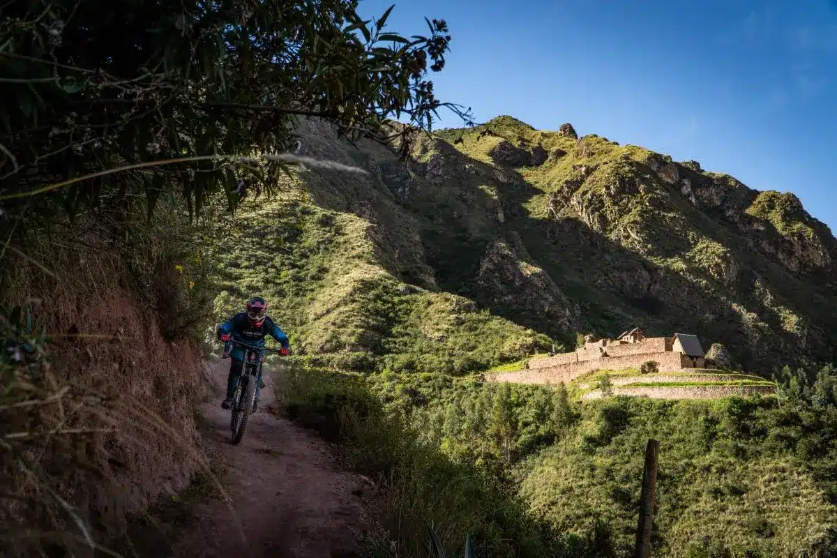 Ciclista descendiendo por un sendero andino rodeado de vegetación rumbo a la cascada inca de Perolniyoc, cerca de Ollantaytambo, Cusco (Peru Biking Tours).