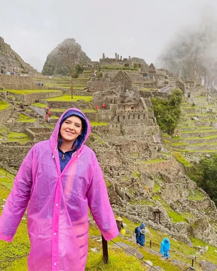 Lleva puesto un impermeable rosado que destaca entre los tonos verdes del paisaje.
