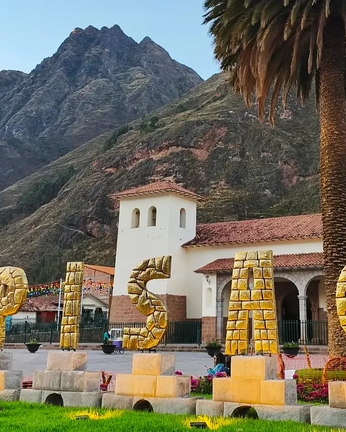 Las letras doradas que forman la palabra “Písac” destacan en primer plano frente a la plaza del pueblo.