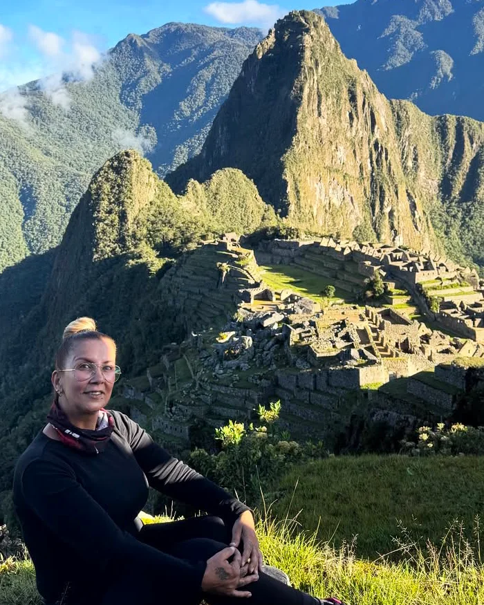 La viajera se encuentra sentada sobre el pasto, disfrutando de una vista privilegiada de Machu Picchu.