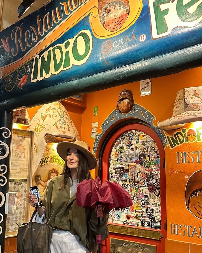 La viajera posa sonriente frente a la colorida fachada del restaurante Indio Feliz en Aguas Calientes.