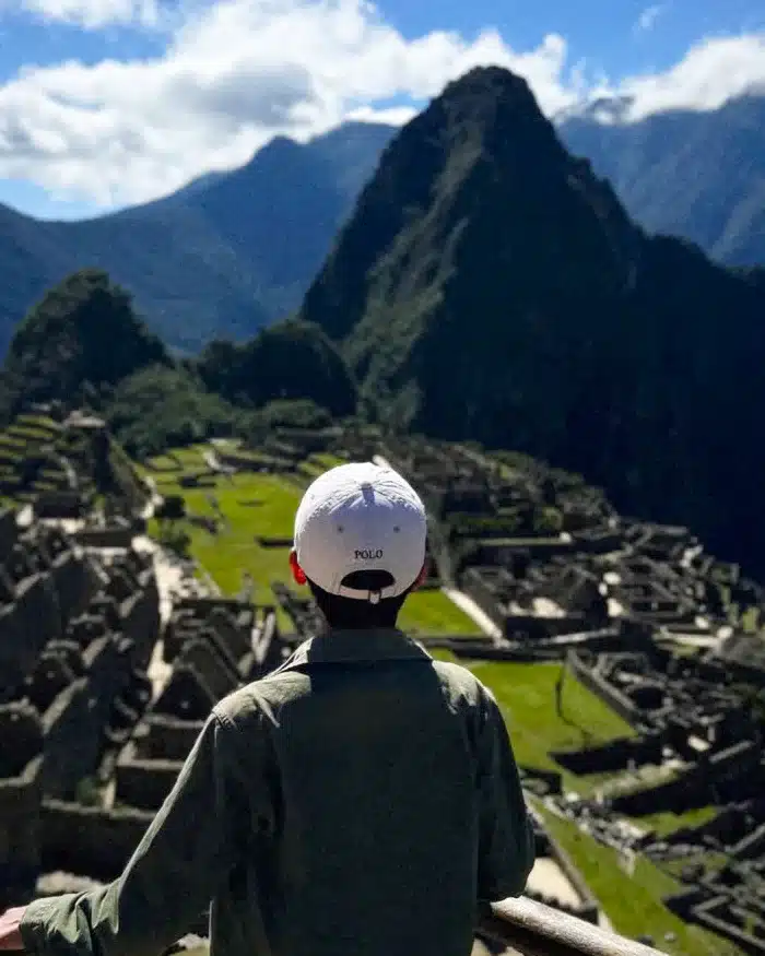 Un viajero contempla Machu Picchu desde un mirador, apreciando la magnitud del sitio arqueológico rodeado de montañas andinas.