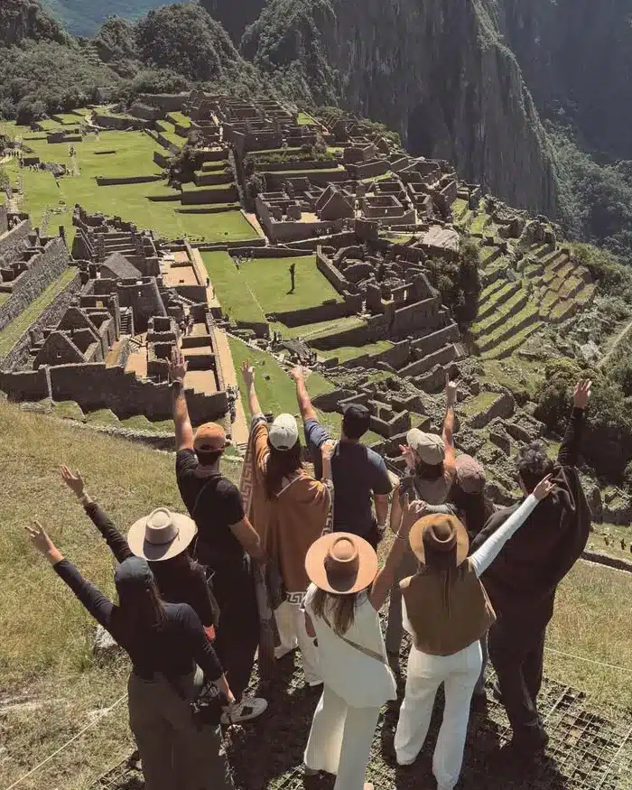 Viajeros frente a Machu Picchu rodeado de montañas verdes y nubes