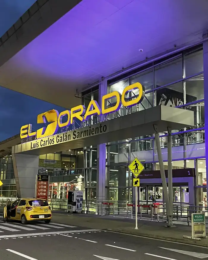 Se observa la entrada del Aeropuerto Internacional El Dorado, con su nombre iluminado sobre la fachada.