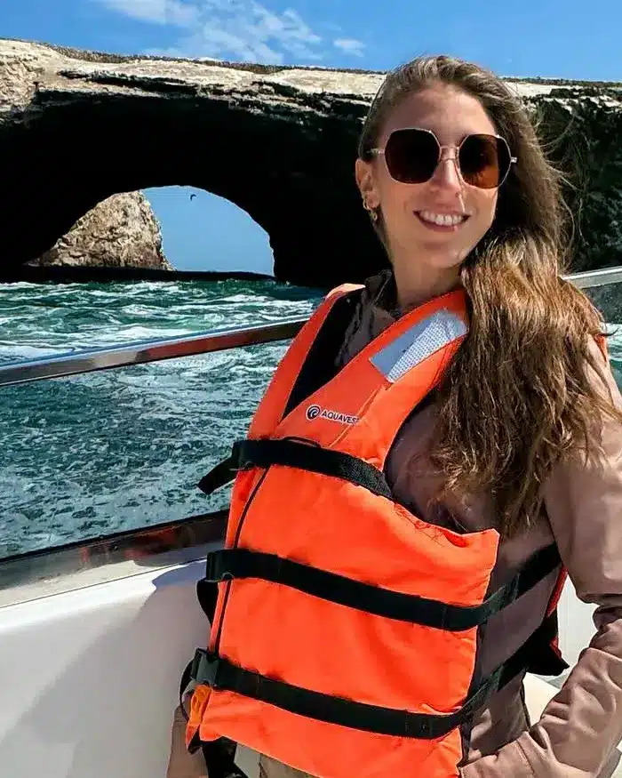 La viajera a bordo de una embarcación, equipada con chaleco salvavidas mientras recorre una zona costera rodeada de formaciones rocosas.