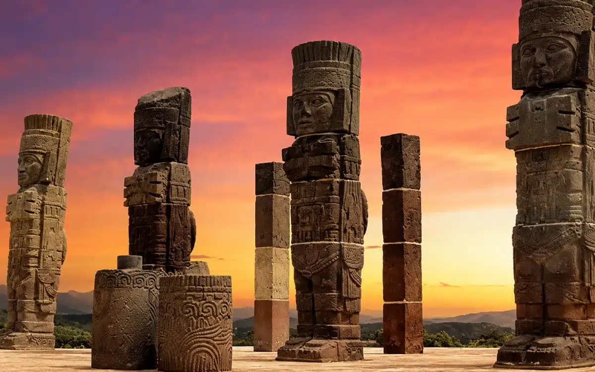 Atlantes de Tula sobre la pirámide tolteca, con columnas de piedra y cielo de atardecer en Hidalgo, México.