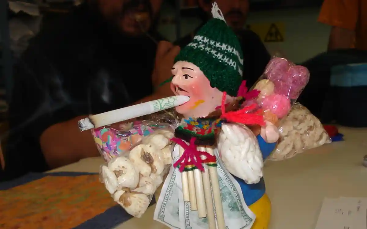 Ekeko con un cigarrillo en la boca, cargado de miniaturas, alimentos y billetes como símbolo de abundancia