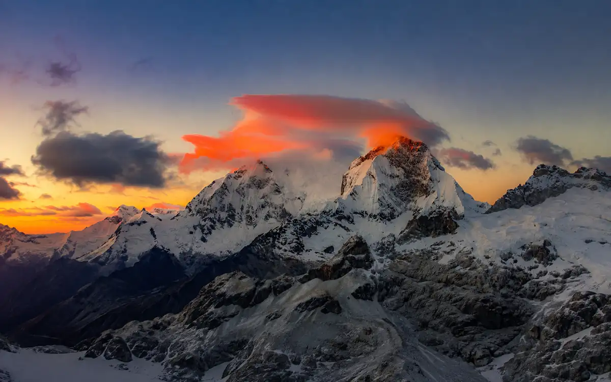 Huascarán rises above the Cordillera Blanca as clouds and sunset light highlight its snow-covered peaks, glaciers and rugged high-altitude terrain in the Peruvian Andes.