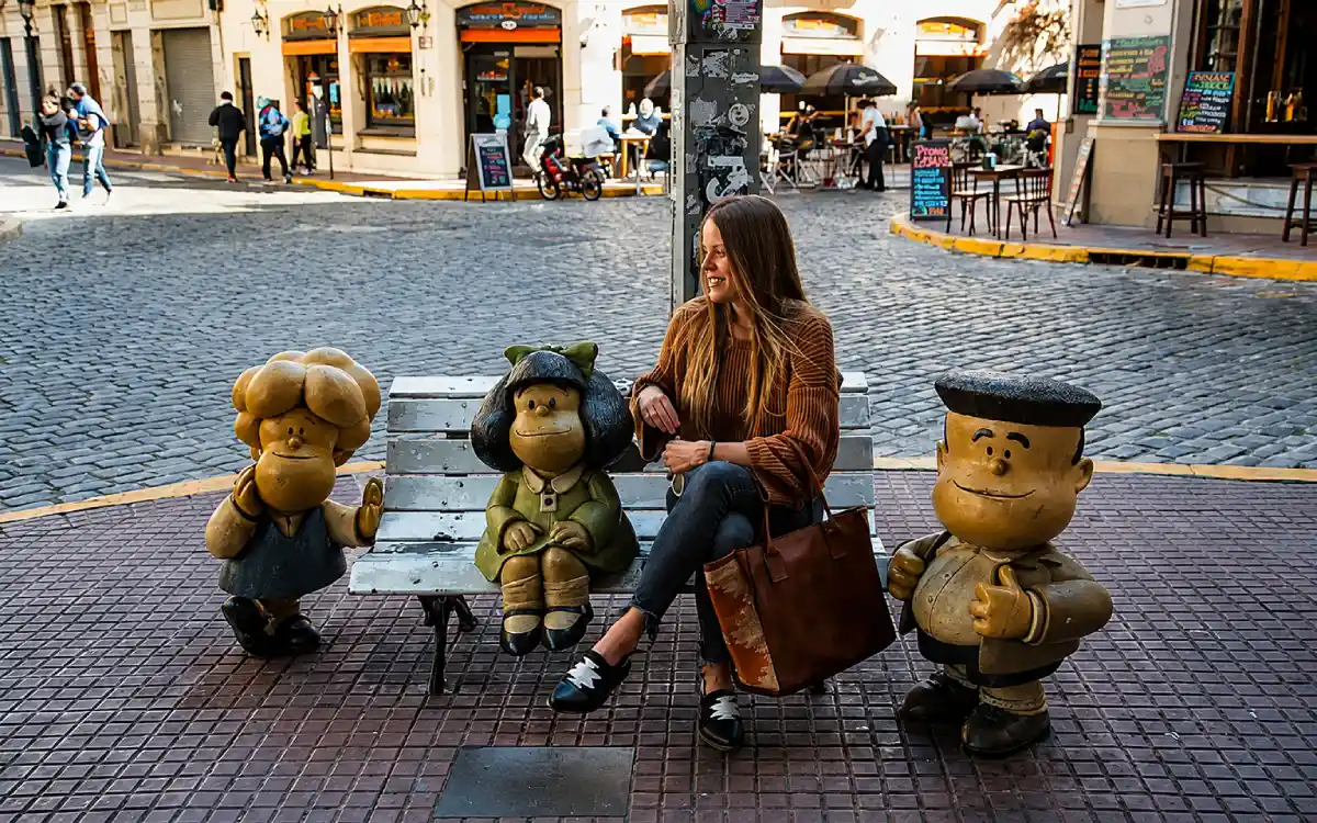 Turista sentada junto a las esculturas de Mafalda, Susanita y Manolito en el Paseo de la Historieta, Buenos Aires.