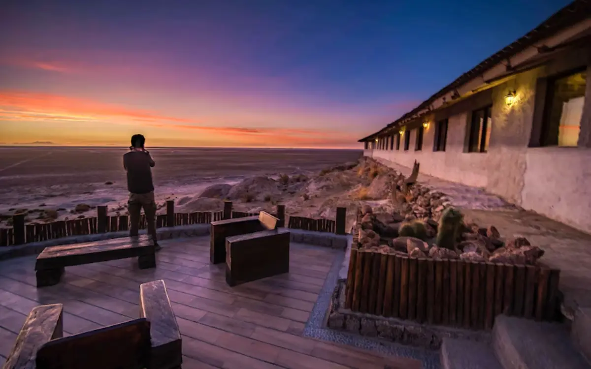Viajero en balcón de hotel cerca del Salar de Uyuni, observando el atardecer con vista panorámica.