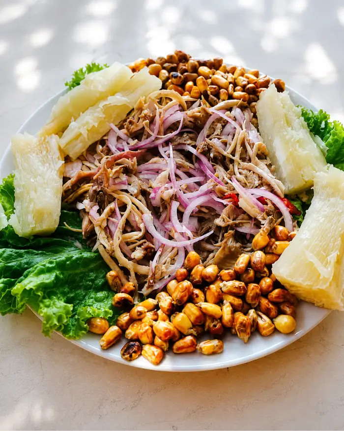 Ceviche de cañán picado servido con yuca, maíz tostado, cebolla morada y lechuga en plato tradicional.