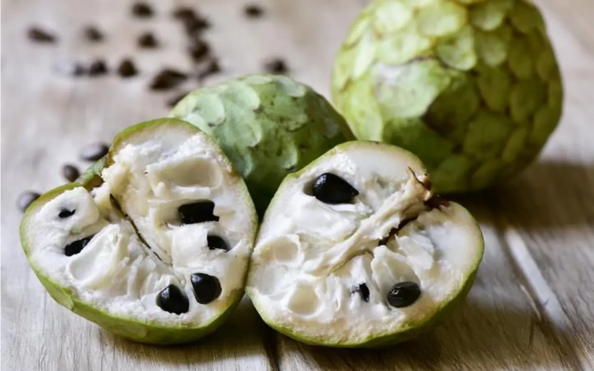 Chirimoyas maduras, una entera y otra cortada, mostrando su pulpa blanca cremosa y semillas negras.