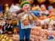 Figura del Ekeko con cigarro, billetes y miniaturas de abundancia en un mercado tradicional andino.