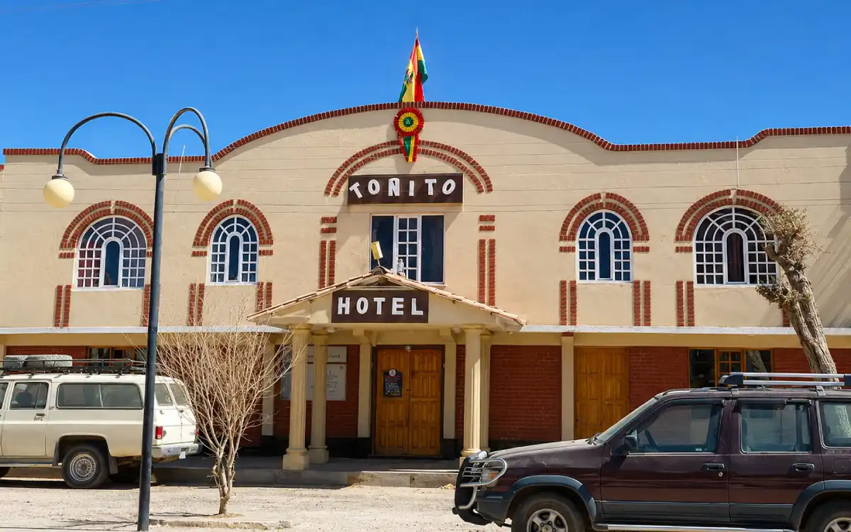 Fachada del hotel Tonito en Bolivia con arquitectura colonial, bandera boliviana, cielo despejado y autos estacionados.
