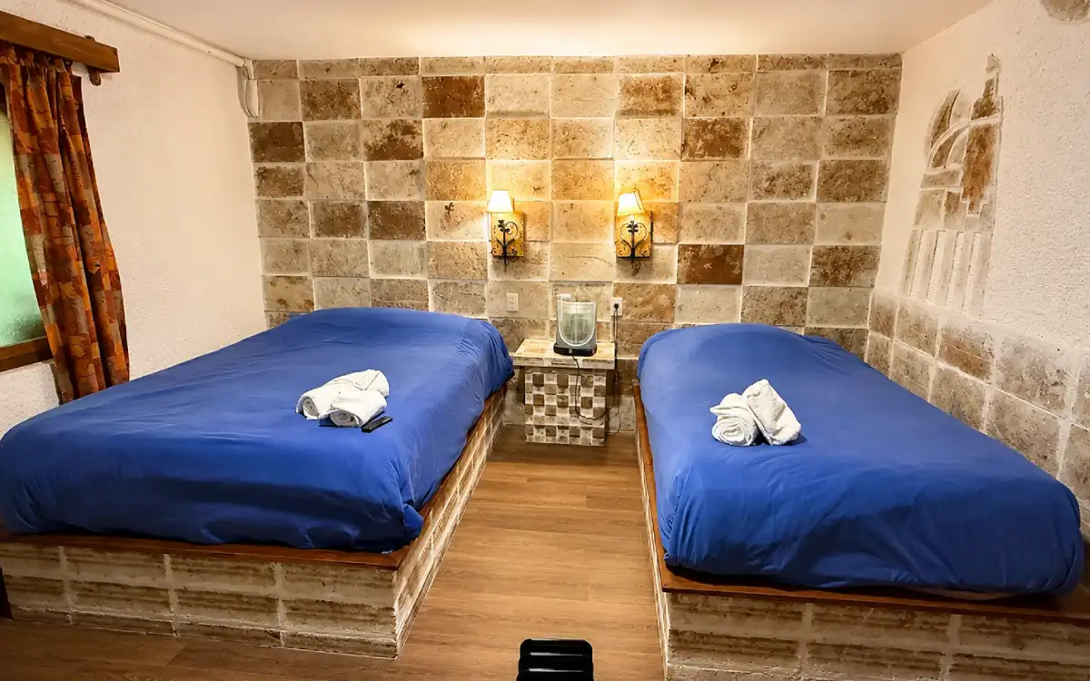 Habitación doble del hotel Tambo Aymara con camas azules, luces cálidas y diseño rústico minimalista.