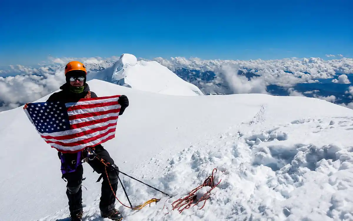 Montañista en la cima del nevado Salkantay sosteniendo una bandera de Estados Unidos,